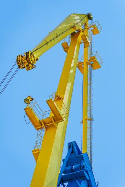 Açık mavi gökyüzüne karşı yükselen parlak sarı turna yapısı mühendislik detaylarını gözler önüne seriyor. Vinç teknolojisi kavramı, ağır makineler, kentsel port altyapısı