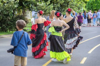 Sokak boyunca insanlarla yürüyen etnik flamenko dansçıları. Parlak elbiseli bir grup flamenko dansçısı park ortamındaki kültür festivalinde kalabalığın arasında yürüyor. İspanyol Kültür Festivali