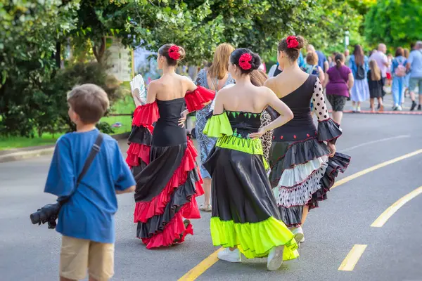 Sokak boyunca insanlarla yürüyen etnik flamenko dansçıları. Parlak elbiseli bir grup flamenko dansçısı park ortamındaki kültür festivalinde kalabalığın arasında yürüyor. İspanyol Kültür Festivali