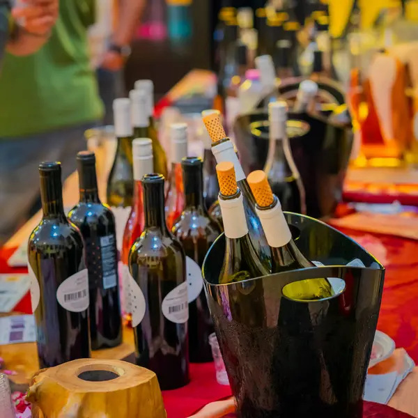 Buz kovasında şişe şarabın yakın çekimi. Şık kovada şarap şişeleri ve arkalarda bulanık kalabalıkla tatma etkinliği masasında düzgünce düzenlenmiş. Şarap sunumu konsepti, kutlama, klas tatma.