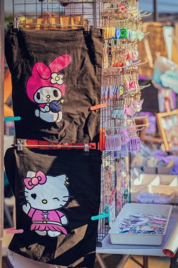 Merhaba Kitty Poşetleri ve Anahtarlıkları. İçinde Hello Kitty ve Melody tasarımlarım olan sevimli siyah çantalar renkli anahtarlıkların yanında sergileniyor. Kawaii modası, şirin aksesuarlar, pop ikonu ürünleri.