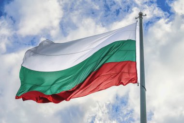 Bulutlu mavi gökyüzünde Bulgar Bayrağı, arka plan. Bulgaristan 'ın ulusal bayrağı rüzgarda sallanarak gurur ve bağımsızlığı simgeliyor. Bulgaristan bayrağı, vatanseverlik, ulusal kimlik, devlet sembolü kavramı