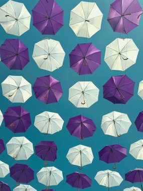 Mavi gökyüzüne karşı havada asılı mor ve beyaz şemsiyeler soyut desenler ve renkli şehir dekorasyonu yaratıyor. Sokak sanatı kavramı, yaratıcı tasarım, yaz kurulumu