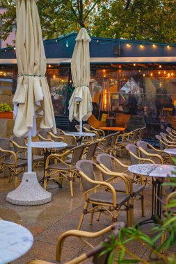Outdoor restaurant patio. Empty cafe terrace with wet chairs and tables under umbrellas after autumn rain. Concept of autumn, rain, end of summer season