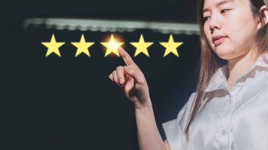 Asyalı bir kadın koyu arkaplandaki beş yıldızı işaret ediyor. Müşteri değerlendirme kavramı.