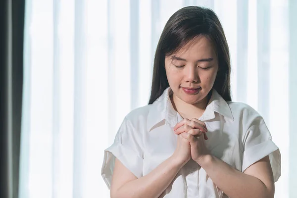 Hopeful make wish, calm asian young woman belief, hand in prayer, sitting meditating on sofa at home, Christian girl praying to God for ask, request with closed eyes dreaming for help, thanks you God.