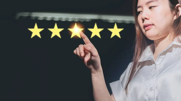 Stock image Asian woman pointing to five stars rating on dark background. Customer review concept.