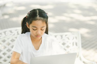 Parktaki çimlerde oturan ve dizüstü bilgisayar kullanan tatlı küçük kız.