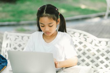 Küçük sevimli Asyalı kız açık kafede otururken dizüstü bilgisayar kullanıyor.