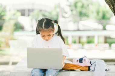 Parktaki çimlerde oturan ve dizüstü bilgisayar kullanan tatlı küçük kız.