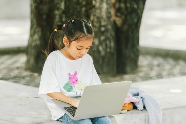 Parktaki çimlerde oturan ve dizüstü bilgisayar kullanan tatlı küçük kız.