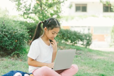 Parkta çimlerin üzerinde dizüstü bilgisayar kullanan tatlı Asyalı kız..