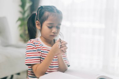 Asyalı küçük kız elinde tespihle evde dua ediyor..