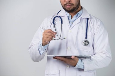 Gri arka planda dururken dijital tablet kullanan erkek doktorun portresi