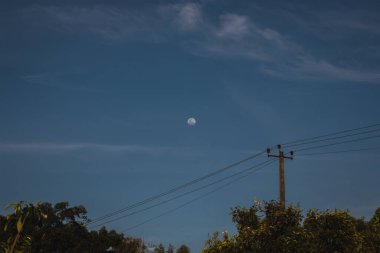 Hindistan 'da elektrik hattı ve elektrik direğiyle mavi gökyüzünde ay var.