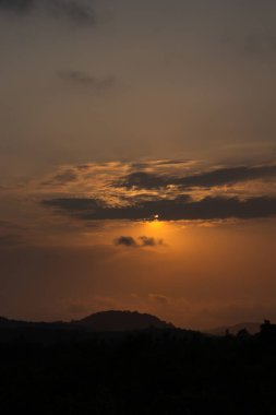 Güneş batıyor, dramatik turuncu bir tonda gökyüzünü boyuyor. Siluetli bulutlar bu huzur dolu parlaklığa karşı oturur ve nefes kesici güzellikte bir manzara yaratır..