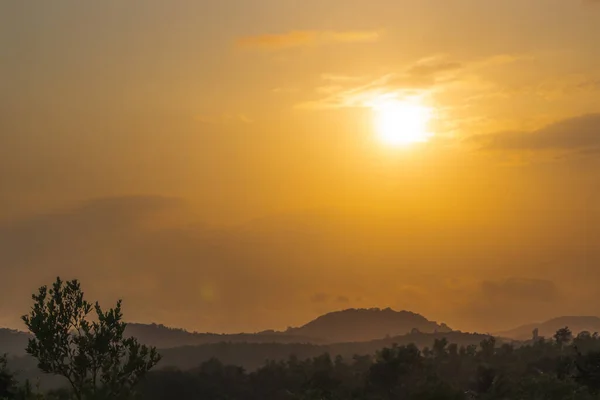 Doğada sakin bir güzellik manzarası, sisli dağlardan ve ağaçlardan yansıyan dramatik turuncu bir gökyüzü. Alacakaranlıkta güneş bu huzurlu topraklarda batarken mükemmel bir parlama..