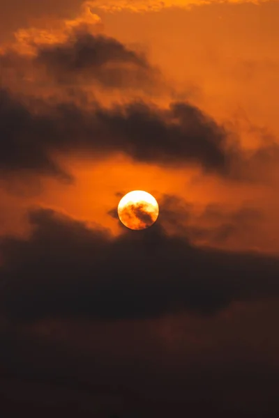 stock image The intense orange afterglow of the sunset casts a dramatic hue over the billowing clouds and bright moon in this awe-inspiring nature scene.