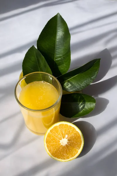 A Glass of orange juice with leaves of the tree and half of an orange with a white background