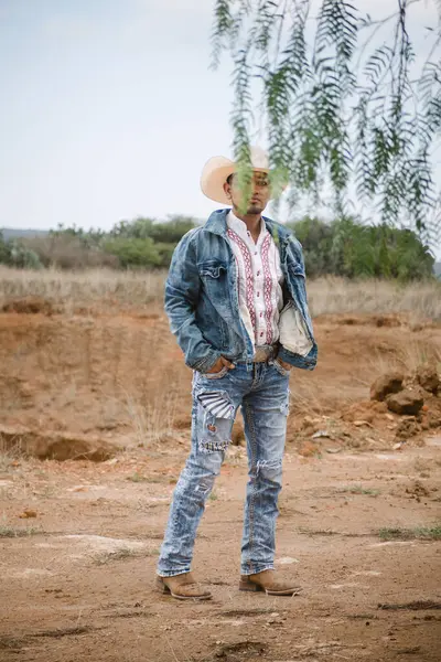 stock image A cowboy wearing jeans and a hat, standing under the sky with fluffy clouds, working on a farm