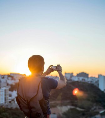 Gün batımında kamerasıyla fotoğraf çeken genç bir adam.