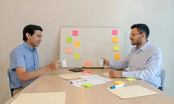 A Two men sitting at a table with a whiteboard and a white board with post it notes