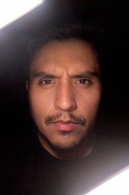 Siyah arka planı ve profesyonel ışıklandırması olan ciddi ve kızgın bir Latin adamın portresi.