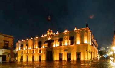 Queretaro, Meksika 'da karanlık bir gökyüzüne karşı aydınlatılan tarihi Casa de La Corregidora' nın güzel gece manzarası. Bu sembolik bina Meksika mirasının ve tarihinin bir sembolüdür. Yapının tepesinde ulusal bayrak gururla dalgalanmaktadır..