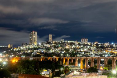 Karanlık gökyüzüne karşı aydınlanan Queretaro su kemerinin çarpıcı gece sahnesi, tarihi ve modern şehir manzarasının karışımını vurguluyor..