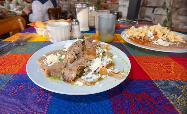 stock image Delicious Mexican dish featuring tender beef rib, refried beans, and fresh tortillas. Vivid tablecloth accents the rustic ambiance, perfect for a cultural dining experience. Ideal for food blogs and culinary marketing.