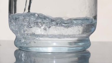 Temiz bir su akıntısı kadehe dolarken büyüleyici kabarcıklar ve kabarcıklar yaratır. Yavaş çekim, suyun hareketinin karmaşık detaylarını ve havayla olan hassas etkileşimini vurgular ve büyüleyici bir gösteriyle sonuçlanır..