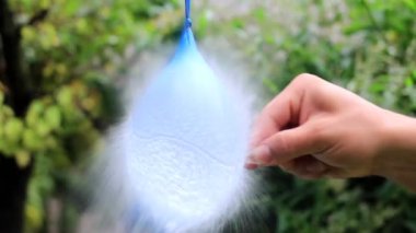 Bir el iğneyle yaklaşırken mavi bir balon bir ipten sarkıyor. Yavaş çekim etkisi balonun gerildiğini ve patlamaya hazırlandığını gösteriyor. Su damlacıkları parıldar ve parıldar. Anın beklentilerini vurgular..