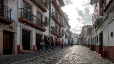 Taxco de Alarcon, Meksika 'da, kaldırım taşlı caddeler, işlenmiş demir balkonlar ve renkli çömlekler ile süslenmiş koloni binalarından geçiyor. Ziyaretçiler, tarihi ortamın tadını çıkararak rahatça dolaşırlar..