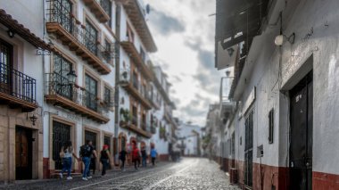 Taxco de Alarcon, Meksika 'da, kaldırım taşı sokaklar güzel korunmuş koloni binalarının arasından geçer renkli çiçeklerle süslenir. İnsanlar geziniyor, bulutlu bir gökyüzünün altında manzaranın tadını çıkarıyorlar..