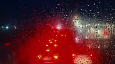 Bulanık şehir ışıklarıyla dolu yağmurlu bir gece canlı bir atmosfer yaratıyor.
