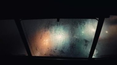 Şehir ışıklarını gösteren yağmura bulanmış ön camlı araçtan gece görüntüsü