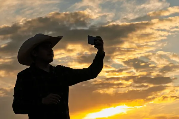Meksikalı vaquero, gün batımında renkli bulutlara karşı bir siluetle selfie çekiyor.