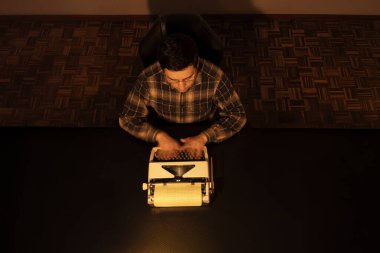 Gözlük takan ve ekose gömlek giyen genç bir adam sıcak ışık altında eski bir daktiloda yazı ve şiir gününe olan aşkını sakin ve odaklanmış bir anda yansıtıyor..