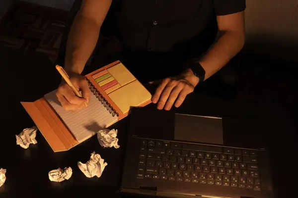 Bir dizüstü bilgisayarın yanına buruşmuş kağıtlarla birlikte bir defter yazan, verimliliği, odaklanmayı ve çalışma ortamındaki yaratıcı zorlukların üstesinden gelmeyi sembolize eden bir kişi..