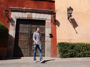 Santiago de Queretaro Tarih Merkezi 'nin kaldırım taşı sokağında gelişigüzel gezinen genç bir adam. Karmaşık demirlerle süslenmiş çarpıcı tarihi bir kapıya yaklaşıyor..