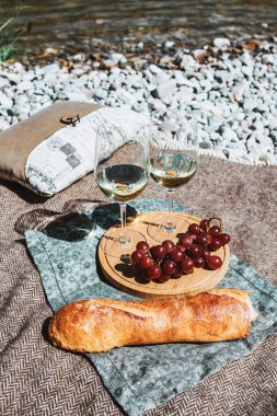 Summer romantic rustic picnic on the coast with white wine glass, baguette, cherries, grape, open book, pillow. Sea beach. Vacation, rest in Europe. Alcohol drink. Inspiration. High quality photo