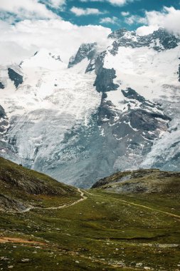 Path among snow mountains. Zermatt, Swiss Alps. Adventure, hiking in Switzerland, Europe. Place for loneliness, silence and relax. Green grass and stones.
