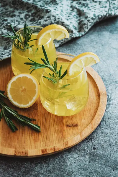 Soğuk kokteylli bardaklar, limonata, dilimlenmiş limon ve beton masada biberiye. Tahta tabak, yakın içkiler, natürmort hayat. Yüksek kalite fotoğraf