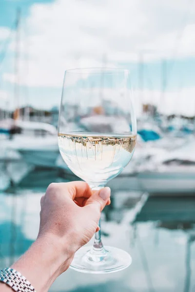 Woman hand with white wine, champagne glass on a yachts, sailing boats, building background. Vacation in Europe. Nice, French riviera, bay. Drink photo. Romantic relax, holiday on the sea coast.