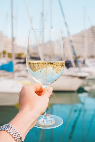 Beyaz şaraplı kadın eli, yatlarda şampanya bardağı yelkenli tekneler, bina geçmişi. Avrupa 'da tatil. Güzel, Fransız Rivierası, Bay. Fotoğraf iç. Romantik rahatlama, deniz kıyısında tatil..