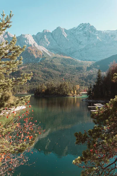 Calm relaxing landscape with Alpine mountains and autumn forest in Bavaria, Germany. Sunny day on the lake Eibsee coast with panoramic view. Vertical photo with mount of Zugspitze