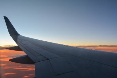 Gün batımında turuncu gökyüzü olan bir uçak kanadını gösteren bir uçak penceresinden görüntü