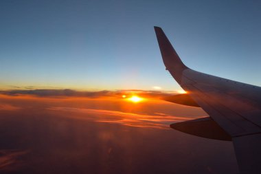 Gün batımında turuncu gökyüzü olan bir uçak kanadını gösteren bir uçak penceresinden görüntü
