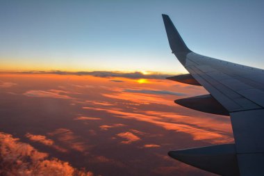 Gün batımında turuncu gökyüzü olan bir uçak kanadını gösteren bir uçak penceresinden görüntü