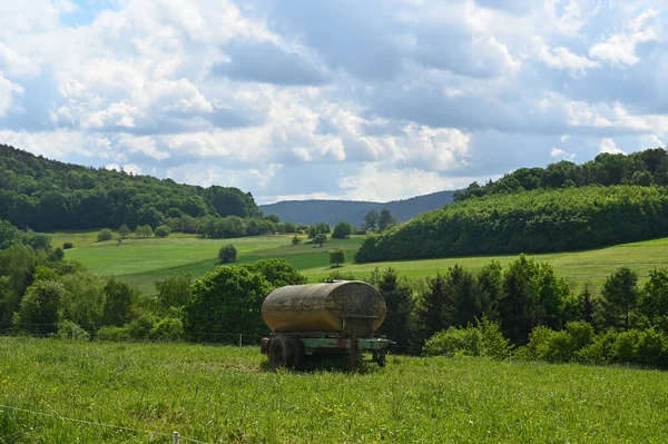 A fertilizer trailer from a farm stands in a field in a green landscape